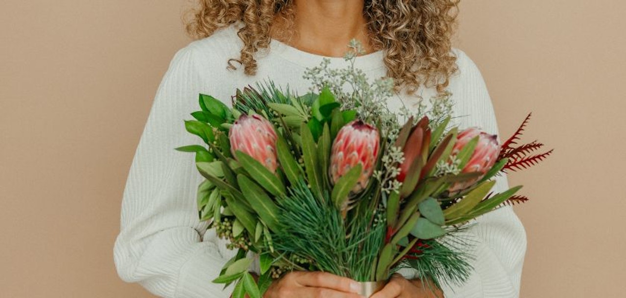 A woman with curly hair holds a vibrant bouquet featuring unique floral elements.