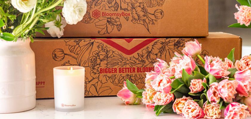 Elegant pink tulips and white blooms arranged beside a candle and BloomsyBox packages.