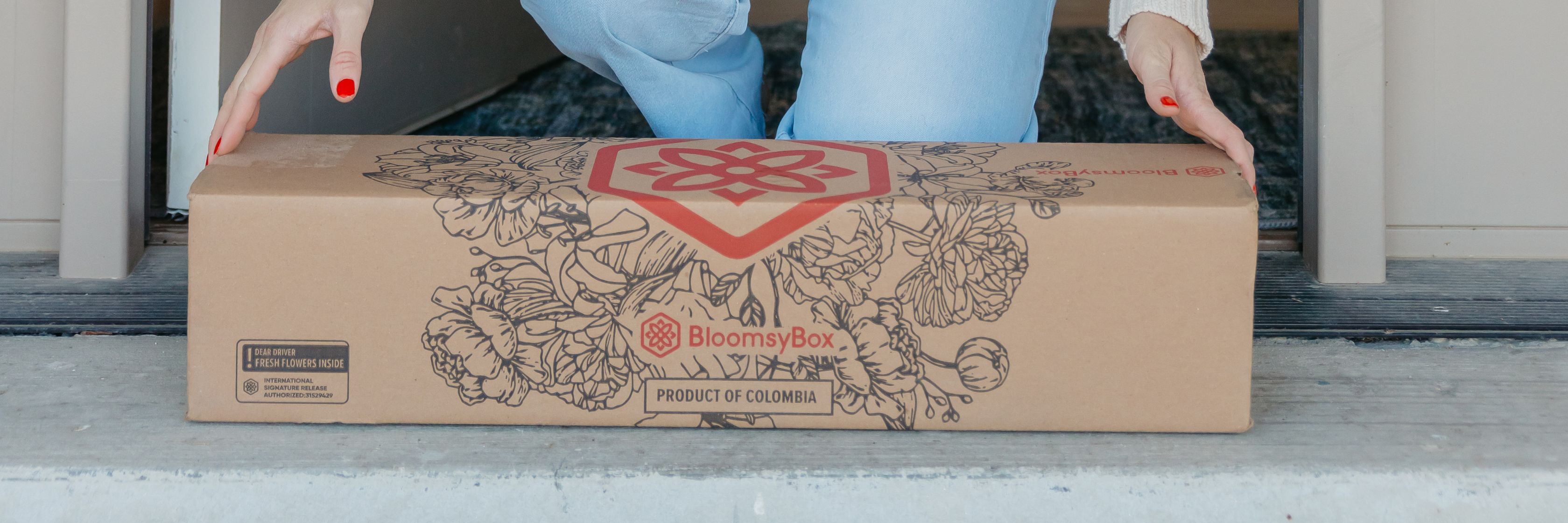 A person carefully placing a BloomsyBox floral delivery on their doorstep.