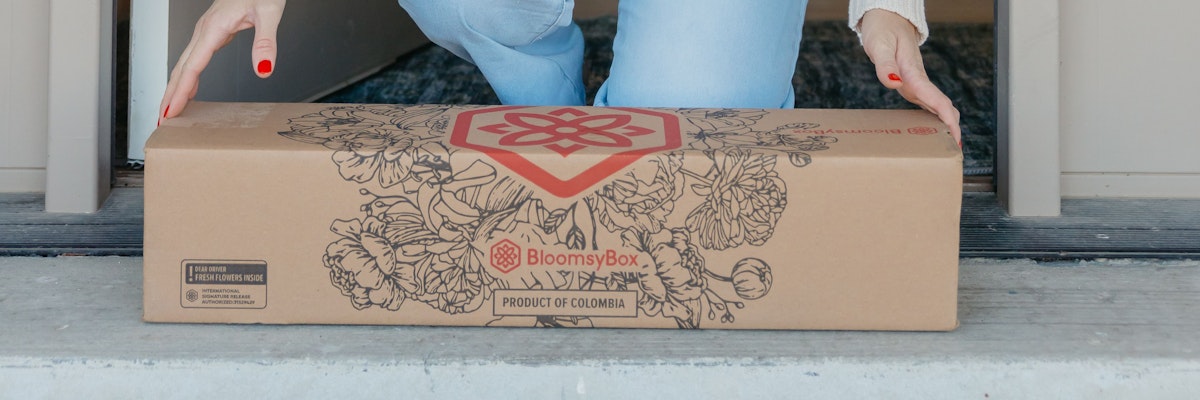 A person carefully placing a BloomsyBox floral delivery on their doorstep.