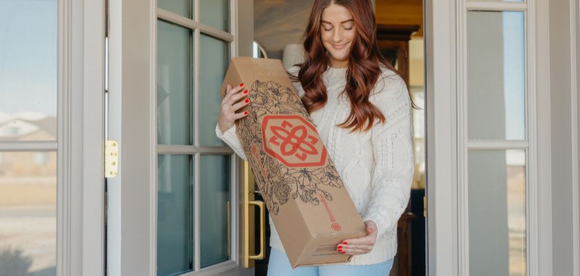 A woman calmly receiving a beautifully designed floral delivery box at her door.