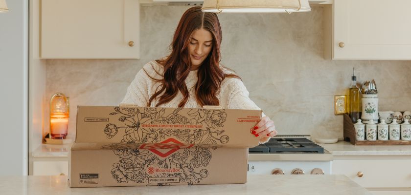 A woman unboxing a beautifully crafted floral arrangement in a cozy kitchen setting.