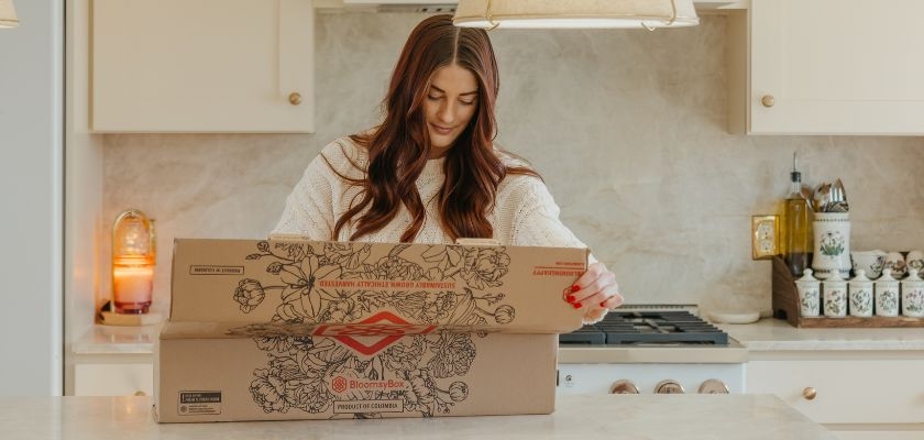 A woman unboxing a beautifully crafted floral arrangement in a cozy kitchen setting.