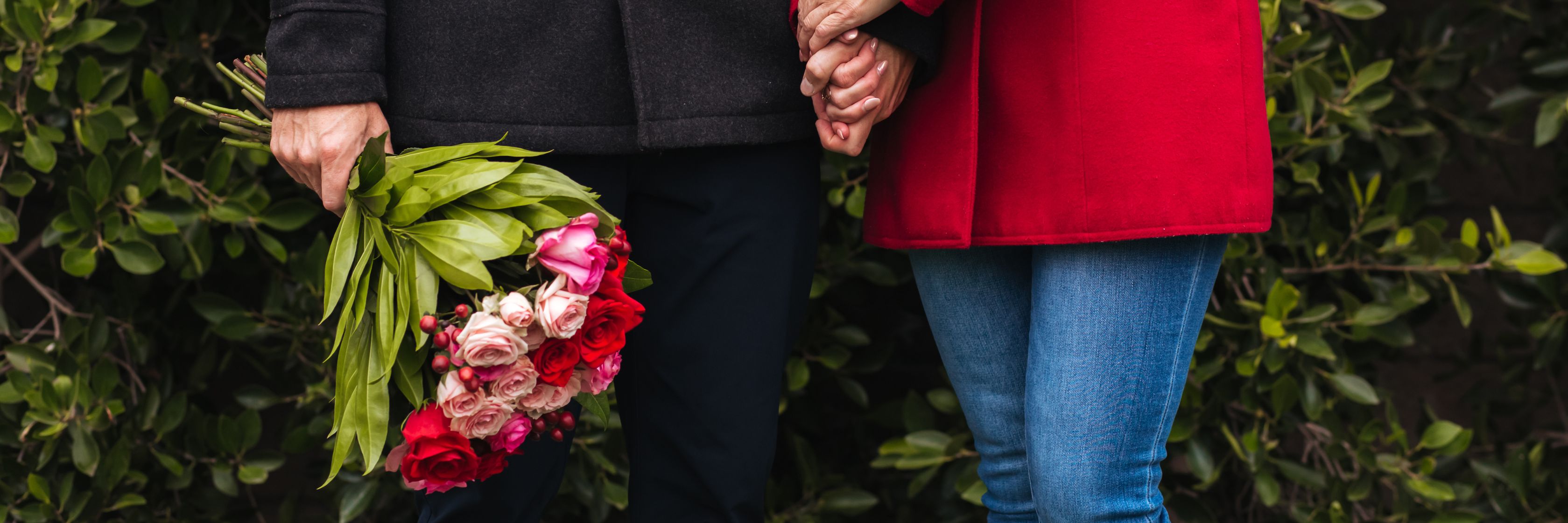 Couple holding hands outdoors, one with a vibrant bouquet of mixed flowers, symbolizing love.