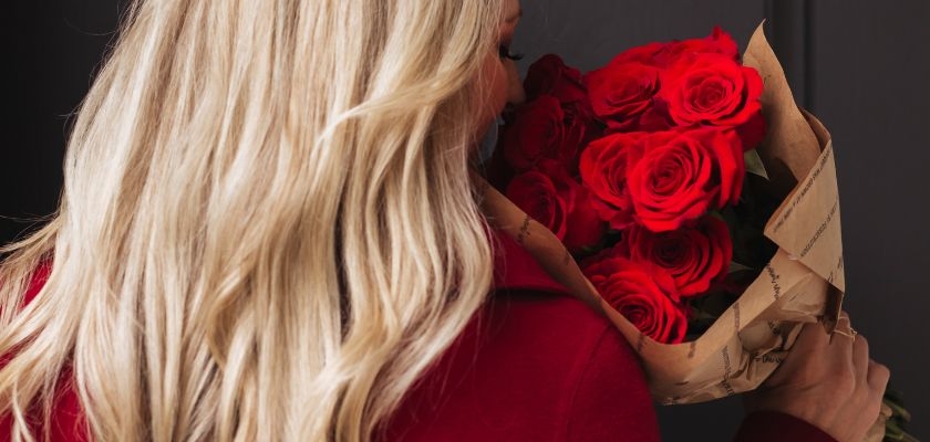 A woman holding a stunning bouquet of vibrant red roses wrapped elegantly for special occasions.
