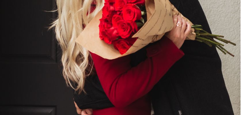 A couple embracing, with a stunning bouquet of red roses held close, celebrating love.