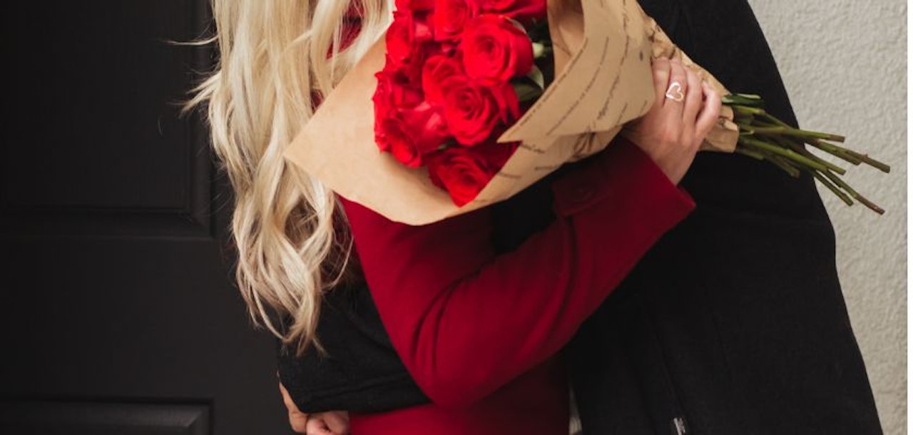 A couple embracing, with a stunning bouquet of red roses held close, celebrating love.