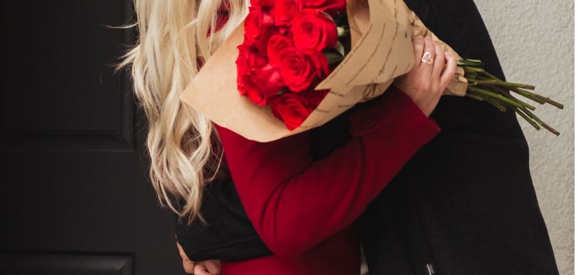 A couple embracing, with a stunning bouquet of red roses held close, celebrating love.