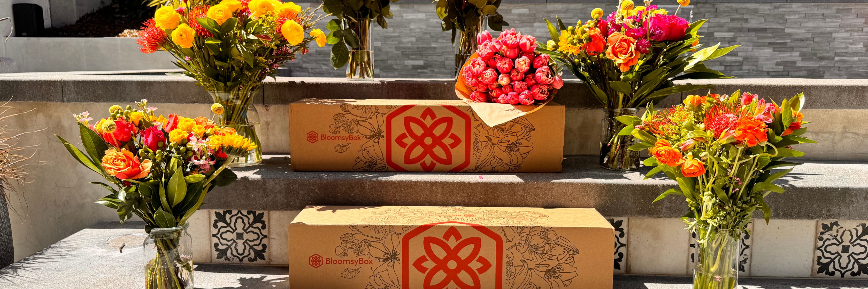 Colorful floral arrangements in vases surround beautifully designed delivery boxes by BloomsyBox.