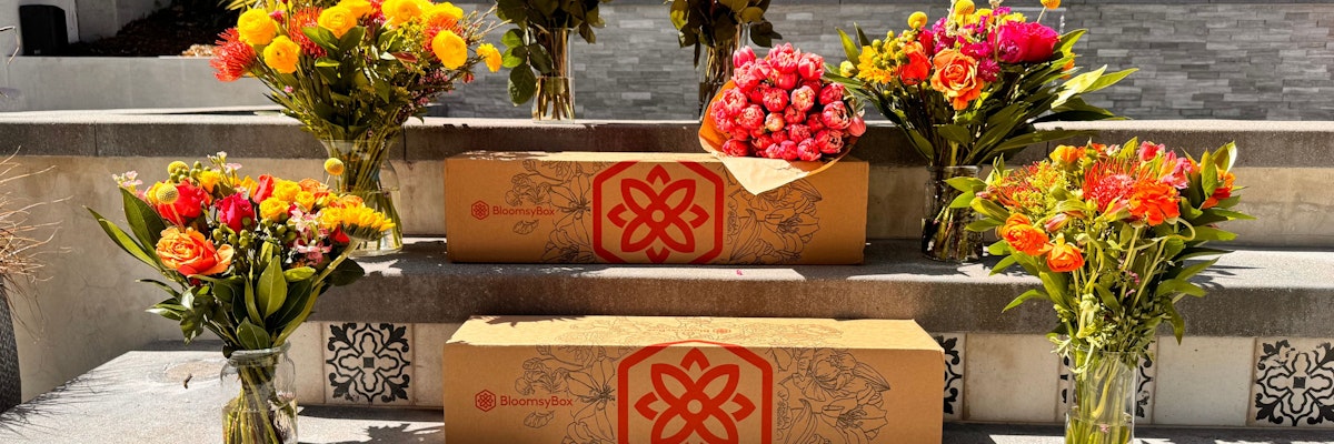 Colorful floral arrangements in vases surround beautifully designed delivery boxes by BloomsyBox.
