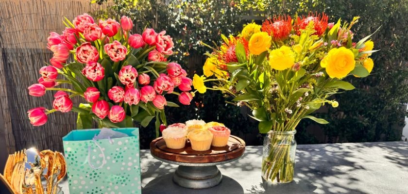Brightly colored tulips and roses in vases, accompanied by a platter of cupcakes.
