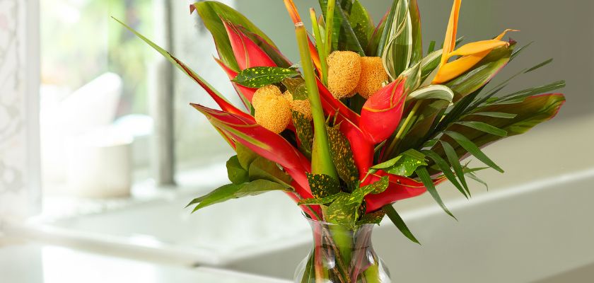 Vibrant floral arrangement featuring tropical blooms and lush greenery in a clear vase.