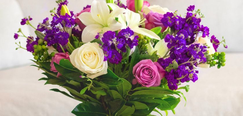 Vibrant floral bouquet featuring white lilies, purple flowers, and pink roses.