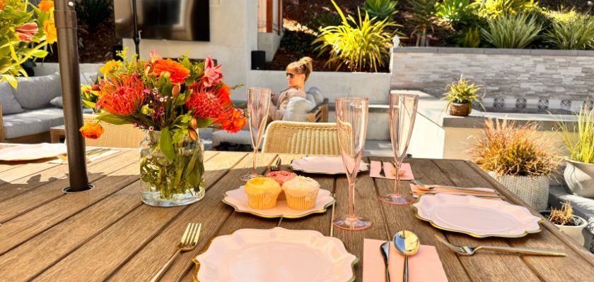 Vibrant outdoor dining setup with colorful flowers, cupcakes, and chic tableware.