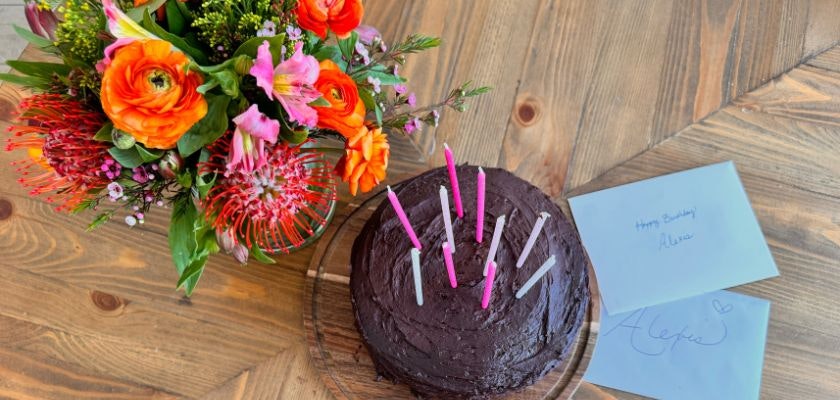 Colorful bouquet with vibrant flowers beside a birthday cake and heartfelt notes.