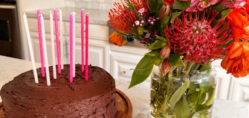 A delicious chocolate birthday cake with colorful candles beside a vibrant floral bouquet.