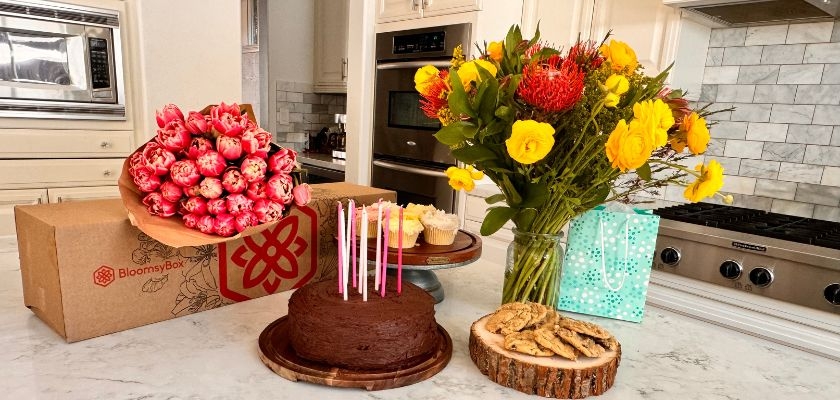 Colorful birthday celebration setup with a cake, flowers, and treats in a cozy kitchen.
