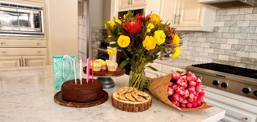 A festive birthday setup featuring a chocolate cake, vibrant flowers, and sweet treats.