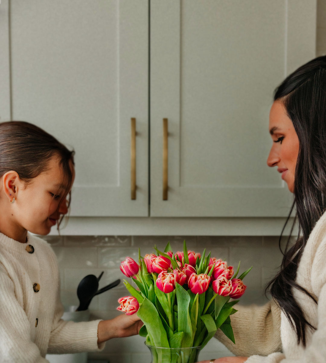 A mother and daughter share a joyful moment with a vibrant bouquet of tulips.