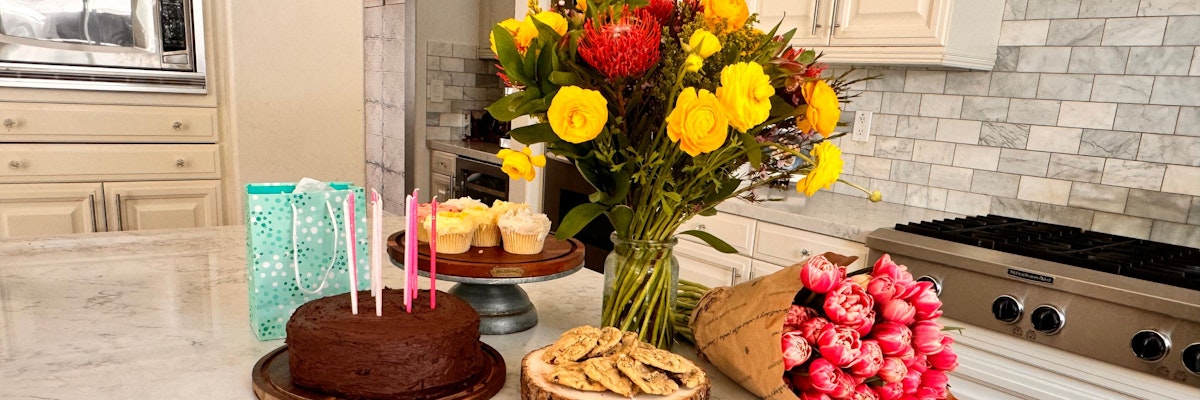 Colorful birthday celebration setting with a cake, flowers, and treats on a kitchen counter.