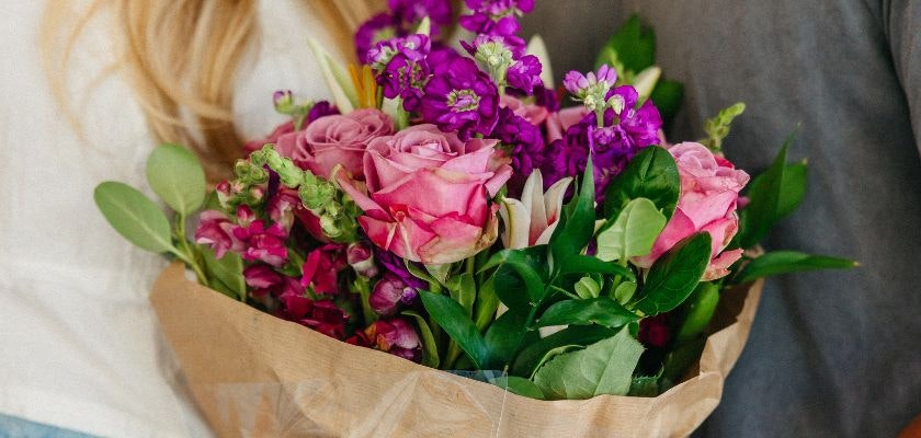 A vibrant bouquet of pink roses and purple flowers wrapped in rustic paper for gifting.