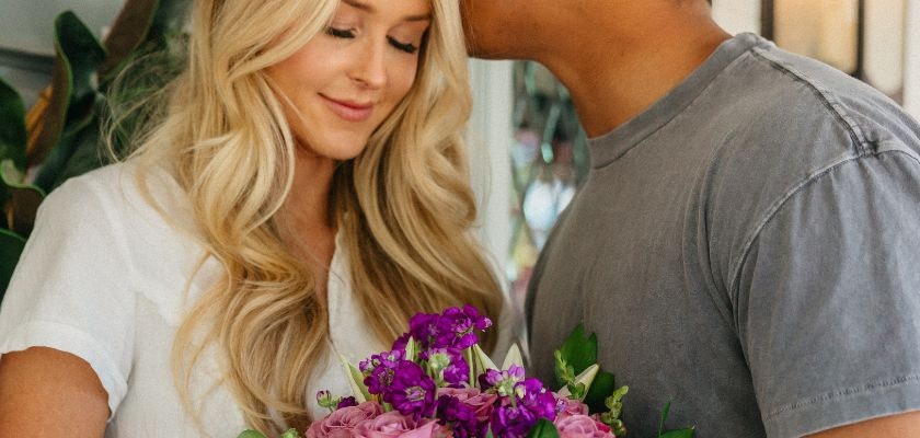A couple sharing a tender moment while holding a vibrant floral bouquet filled with purple flowers.