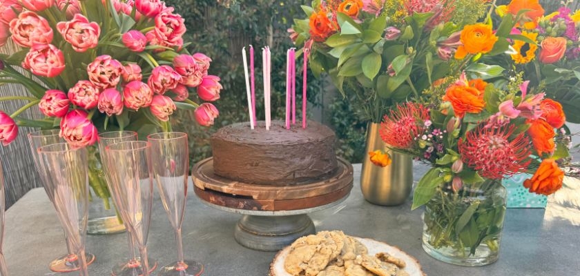 Elegant table setting with a chocolate cake, vibrant flowers, and festive decorations.