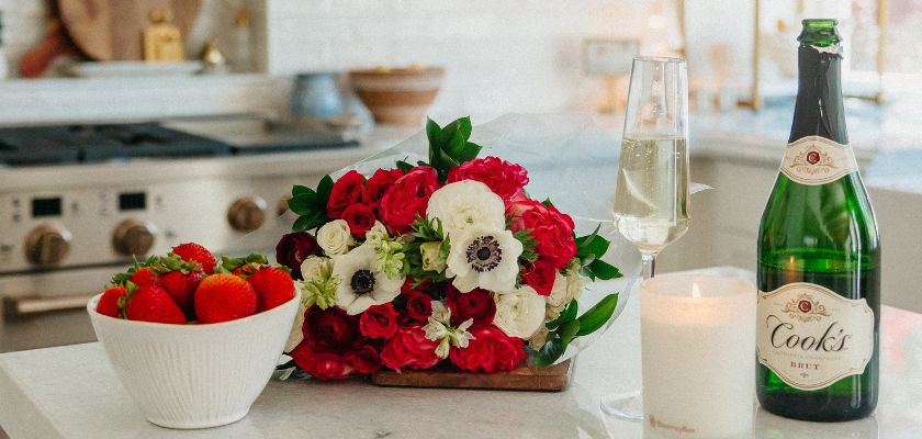 Vibrant floral arrangement with red and white flowers, accompanied by champagne and strawberries.