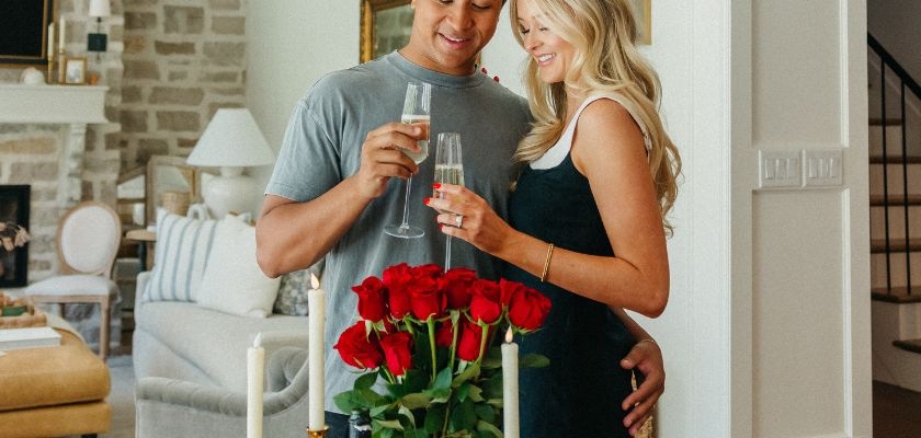A couple toasting with champagne glasses next to a romantic red rose centerpiece.