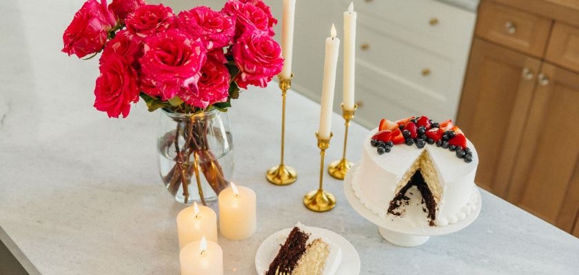 Vibrant pink roses in a vase, a white cake adorned with berries, and elegant candles.