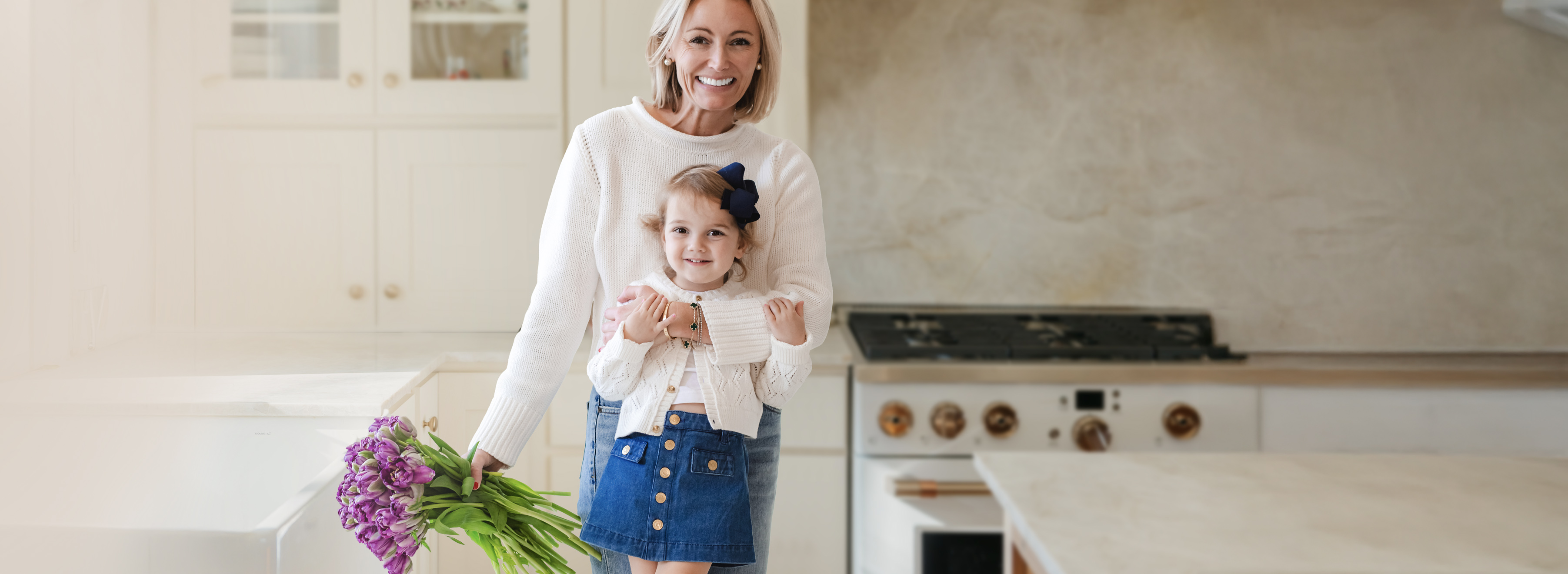 A joyful woman and smiling girl holding a vibrant bouquet in a bright kitchen setting.