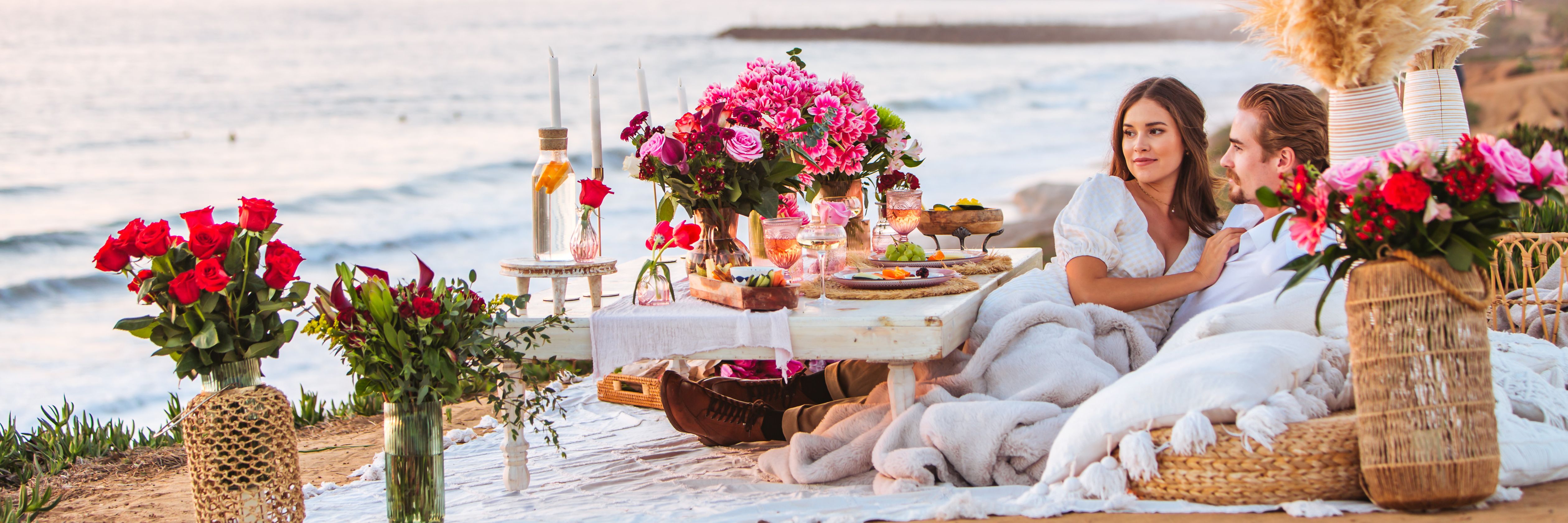 A romantic seaside picnic setup with flowers, snacks, and a cozy atmosphere for couples.