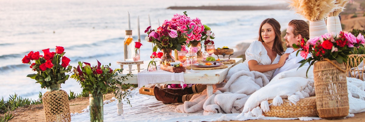 A romantic seaside picnic setup with flowers, snacks, and a cozy atmosphere for couples.