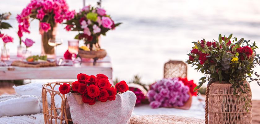 Vibrant floral arrangement featuring red roses, pink blooms, and lush greenery by the beach.