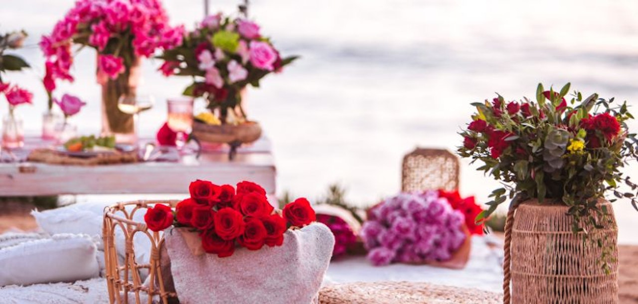 Vibrant floral arrangement featuring red roses, pink blooms, and lush greenery by the beach.