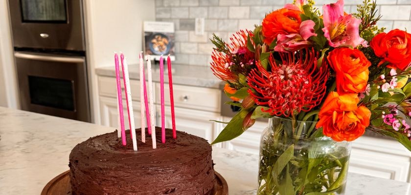 A delicious chocolate birthday cake adorned with vibrant flowers and candles.