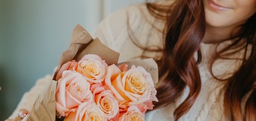 A charming bouquet of blush and peach roses wrapped in brown paper, held by a woman.