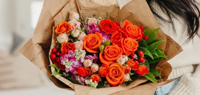 Vibrant bouquet featuring orange roses, pink blooms, and lush greenery in elegant wrapping.