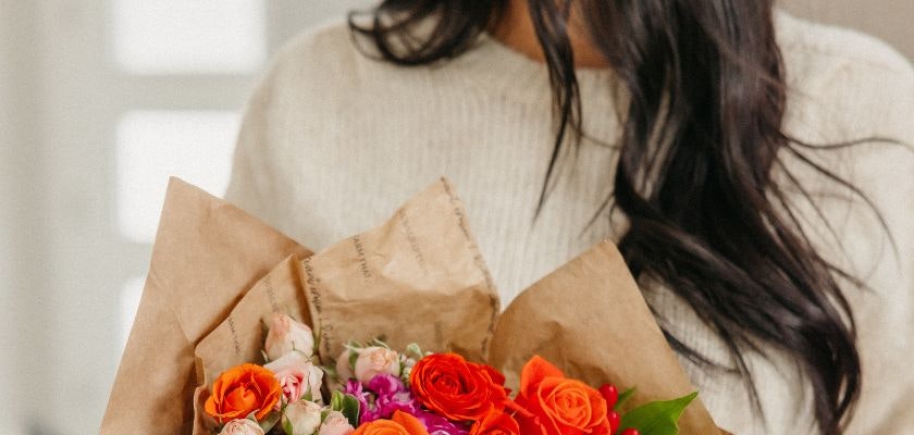 A vibrant bouquet of orange and pink roses and delicate blooms, wrapped in eco-friendly paper.