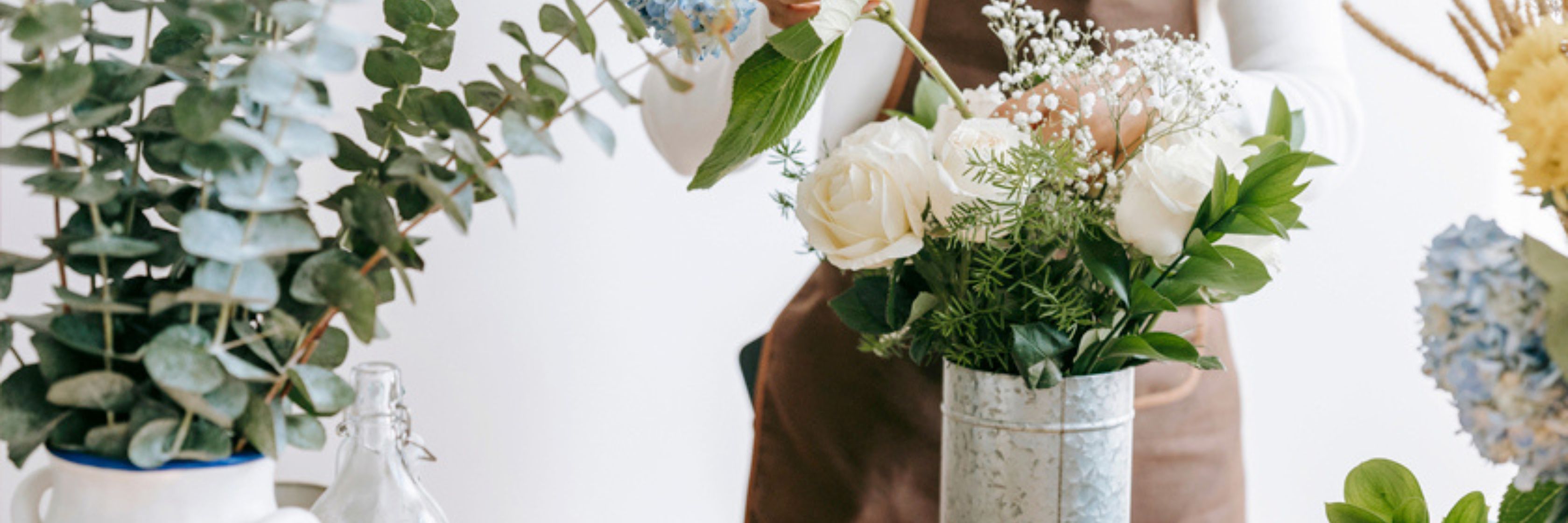 A florist arranging a delicate bouquet of white roses and greenery in a stylish vase.