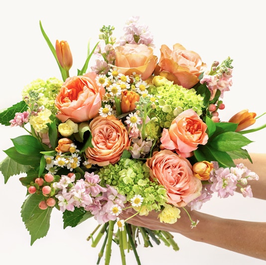 Vibrant floral bouquet featuring peach roses, green blooms, and delicate blossoms, elegantly arranged.