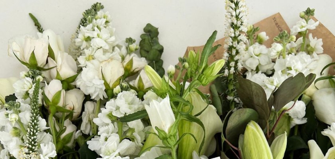 Elegant white floral arrangement featuring roses, lilies, and seasonal greenery in a stylish bouquet.