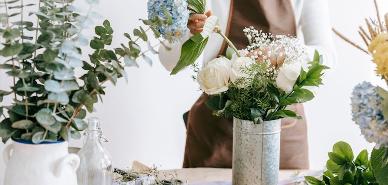 A florist arranging delicate white roses and blue hydrangeas in a charming vase.