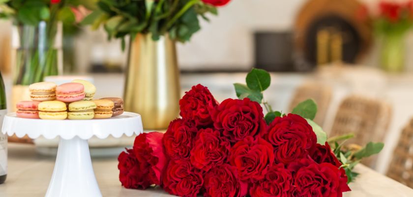 Lush red roses arranged elegantly beside colorful macarons in a bright, inviting setting.