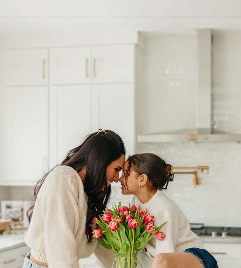 A joyful moment between two friends sharing laughter over a vase of vibrant tulips.