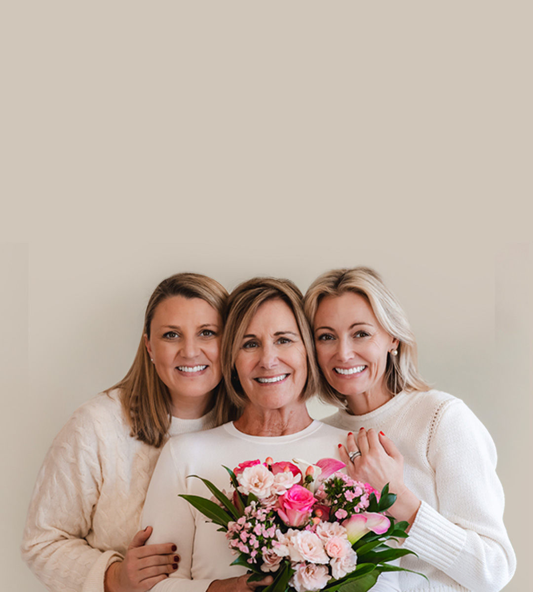 Three smiling women in cozy sweaters hold a beautiful floral bouquet together.