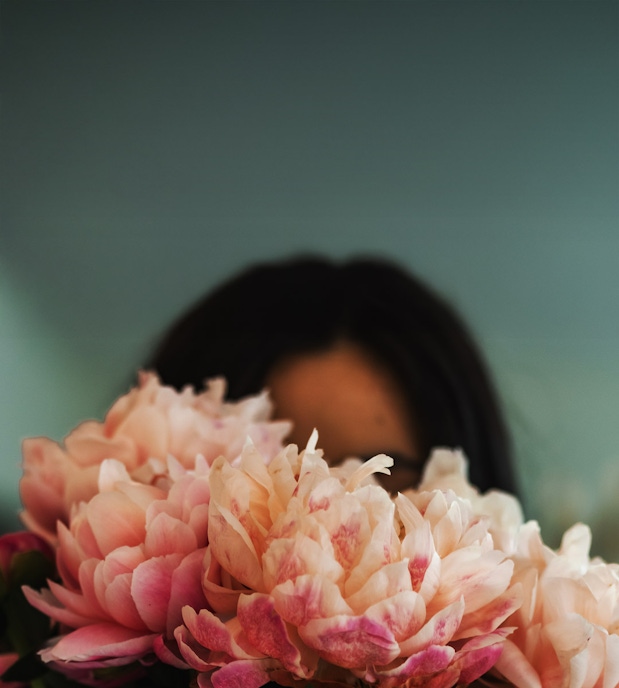 A person partially hidden behind a stunning bouquet of pink peonies, radiating beauty.