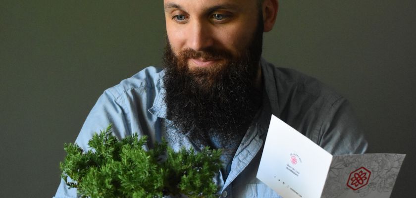 A man admiring a small potted plant, accompanied by a greeting card, creating a thoughtful gift moment.