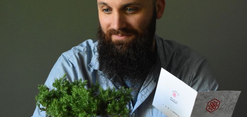 A man admiring a small potted plant, accompanied by a greeting card, creating a thoughtful gift moment.