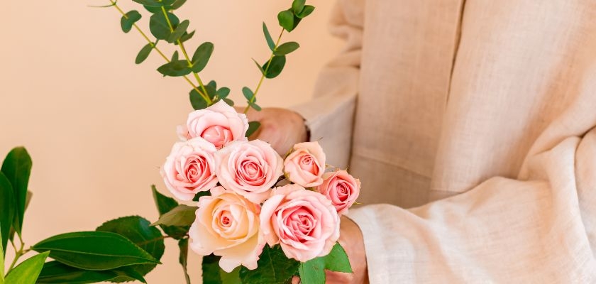 Soft pink roses held delicately in a person's hands, surrounded by lush green leaves.